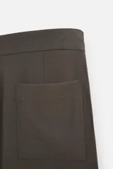 Pantalón marrón oscuro de corte amplio, con cintura ajustable con cordón, bolsillos plastrón delanteros y traseros, detalle de costuras frontales y cierre frontal con cremallera y gancho metálico oculto.