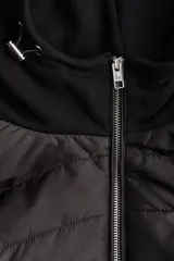 Campera negra híbrida con cuerpo acolchado y mangas de punto. Tiene capucha con cordones ajustables, cierre frontal, bolsillos laterales con botón a presión y puños acanalados.