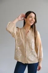 Camisa color beige con bordados florales blancos, cuello mao, mangas largas con elástico en los puños y cierre frontal con botones.