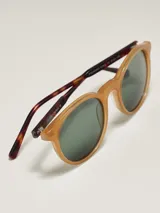 Lentes de sol de montura redonda en tono marrón rosado translúcido, con lentes oscuros degradados de negro a gris claro.