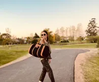 Bolso de viaje grande de cuero vacuno color negro con detalles en marrón. Tiene herrajes metálicos, gran superficie interna, asa de mano y correa para el hombro.