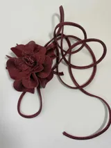 Accesorio color bordo con forma de flor, hecho de cuero. Puede usarse como colgante, faja o gargantilla.