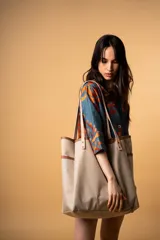 Bolso tipo tote bag de lona impermeable color beige con asas de cuero marrón, bolsillo interior y cierre superior.