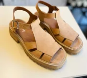 Sandalias de cuero color beige con tiras entrecruzadas y hebilla lateral.