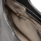 Bolso tipo hobo o media luna de cuero sintético negro texturizado, con costura central vertical en hilo blanco. Incluye asa corta fija y una correa larga desmontable tejida con patrón de espiga en blanco y negro. Posee herrajes metálicos dorados y un logo metálico con la inscripción "XL" en el frente.