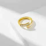 Anillo dorado con diseño abierto, con una pieza rectangular de nácar en un extremo y una hilera de circonitas rectangulares en el otro.