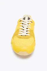 Zapatillas deportivas amarillas con detalles en gamuza y malla, cordones blancos y suela color caramelo.