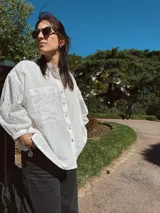Camisa blanca de broderie y tusor, corte holgado, con cuello mao, mangas largas abullonadas con puños elásticos, cierre frontal con botones y bolsillo de parche en el pecho.