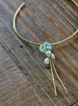 Gargantilla rígida dorada con dije colgante de piedra irregular azul y blanca, perlas y cuentas de vidrio.