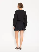 Minifalda negra confeccionada en lycra doble, con cierre lateral y tiracierre en tela base. Tiene doble capa de volados caracol en el ruedo y tajo con moño en tela complemento.