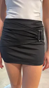 Minifalda negra con frunce lateral y detalle de hebillas metálicas.