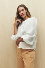 Camisa color crema a rayas verticales finas, de cuello mao, mangas 3/4 abullonadas con elástico en los puños y cierre frontal con botones de nácar.