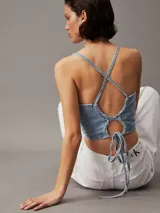 Top corto de denim rígido de algodón celeste, con cuello alto, espalda abierta con cierre anudado y logo de Calvin Klein en el bajo.