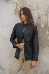 Camisa negra de cuero ovino con cuello mao, cierre frontal con botones a presión, dos bolsillos de parche en el pecho y tachas doradas en cuello, bolsillos y mangas.