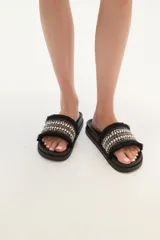 Sandalias tipo slider blancas, con tira ancha decorada con trenzado de hilo beige y plateado, tachas piramidales plateadas y flecos blancos en los bordes.
