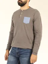 Remera manga larga gris con cuello abotonado y bolsillo azul en el pecho.
