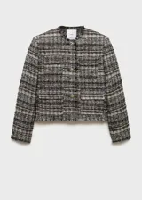 Conjunto de chaqueta y falda de tweed en tonos blanco, negro y dorado. La chaqueta es corta con cuello redondo, botones metálicos y bolsillos de parche. La falda es mini con abertura lateral y detalle de lazos.