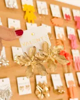 Aretes colgantes dorados con diseño de flor grande y pétalos texturizados, tipo statement.