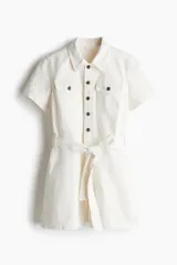 Mono corto color blanco de denim rígido, con cuello camisero, cierre abotonado, mangas cortas, bolsillos superiores con botón y cinturón extraíble.
