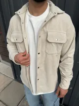 Sobrecamisa de pana color beige con cuello clásico, cierre frontal con broches metálicos a presión, dos bolsillos de parche en el pecho con solapa y puños abotonados.