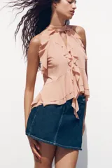 Top color rosa viejo de cuello halter ajustable con lazadas. Detalle de abertura en el delantero y volantes en el mismo tejido.