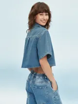 Camisa de denim celeste con corte cropped, mangas cortas y bolsillo en el pecho.
