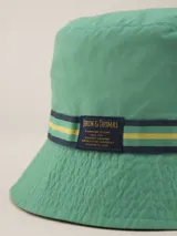 Gorro tipo bucket color mostaza con cinta decorativa a rayas horizontales en tonos bordó, amarillo y azul marino.