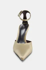 Zapato de tacón alto fino, color dorado, con cuerpo satinado, punta fina y pulsera al tobillo con hebilla metálica.