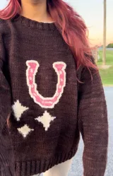 Sweater marrón tejido a mano con diseño de herradura fucsia y estrellas crudas.