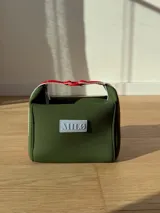 Neceser color beige de forma rectangular, con cierre superior y asa de mano.