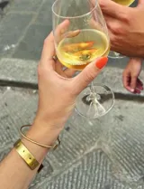 Pulsera dorada tipo brazalete rígido con perforaciones y pulsera dorada fina con dije de piedra blanca.