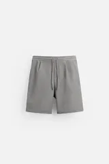 Bermuda gris de corte recto, con cintura elástica ajustable con cordón, pliegues frontales, bolsillos laterales y bolsillos traseros de vivo.