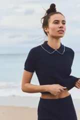 Top de punto blanco con rayas horizontales azul marino, cuello solapa y manga corta.