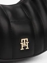 Cartera de hombro cruzada negra con diseño acolchado, silueta curva, insignia del monograma TH dorada, cierre de cremallera, correa ajustable, compartimento principal y bolsillo interior abierto.