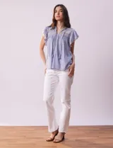 Blusa blanca de algodón con cuello a la base y escote en V con lazo de ajuste. Tiene mangas cortas con terminación amplia y bordados en delantera, mangas y espalda.