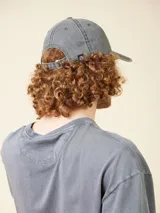 Gorro de gabardina gris oscuro con visera curva, ajustable en la parte trasera con hebilla metálica. Presenta bordado frontal con el logo de la marca y el año 1985.