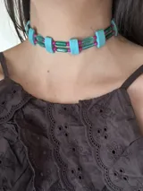 Gargantilla corta con cuentas de piedra color turquesa, ojos de tigre color marrón, resina color verde y cristales facetados color rosa. Se cierra con cadena de acero quirúrgico y ganchito para ajustar.