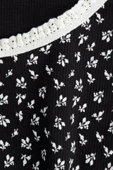 Top corto de manga corta, ajustado al cuerpo, con estampado floral pequeño en blanco sobre fondo negro. Presenta ribete de encaje blanco en el escote redondo y en los bordes de las mangas. El cuerpo principal parece ser de tejido acanalado.