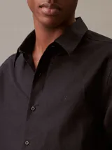 Camisa negra de lino y algodón, de corte clásico, con cuello en punta, cierre frontal con botones y mangas largas con puños abotonados.