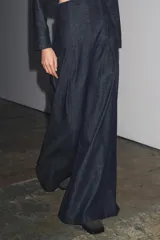 Pantalón de jean azul oscuro, de tiro muy alto y pierna ancha. Presenta pinzas en la parte delantera y cierre trasero con cremallera oculta.