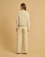 Chaleco corto color beige, con cuello redondo, cierre frontal con un botón y dos bolsillos delanteros.