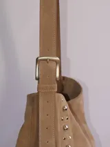 Bolso tipo bandolera de cuero negro con flecos y tachas plateadas. Tiene correa regulable, forro interior y bolsillo interno.