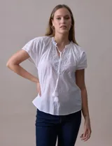 Blusa blanca de algodón marca Cupio, con cuello a la base, escote en V y lazo de ajuste. Presenta bordado en la parte delantera y mangas cortas amplias con aplique de puntilla.
