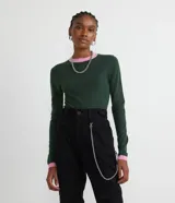 Blusa de punto verde con cuello redondo y mangas largas. Presenta detalles contrastantes en color rosa en el cuello y los puños.