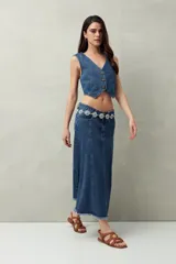 Falda midi de denim negro con tiro bajo, corte evasé, costuras verticales y ruedo desflecado.