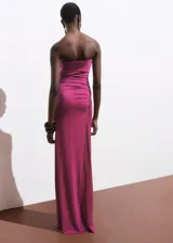 Vestido largo fucsia sin mangas, con escote strapless, corte ajustado y frunces laterales. Presenta abertura en un lateral. Ideal para eventos formales.