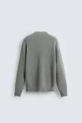 Sweater gris de punto con cuello en V, manga larga y terminaciones irregulares con efecto desgastado.