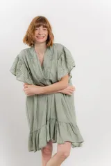 Vestido corto color beige confeccionado en algodón, con escote en V con detalles bordados, mangas cortas amplias con volados y falda con ruedo en volado.