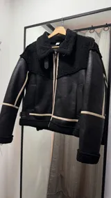 Campera negra de cuero con interior de piel sintética blanca, cierre frontal con cremallera, cuello con solapas y bolsillos laterales.