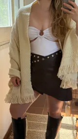 Minifalda negra de cuero sintético con detalle de ojales metálicos en la cintura.